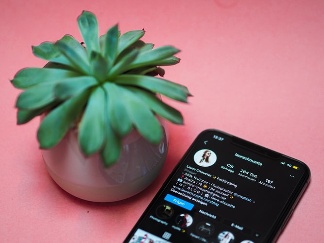 an iphone on a pink table, with a green plant next to it